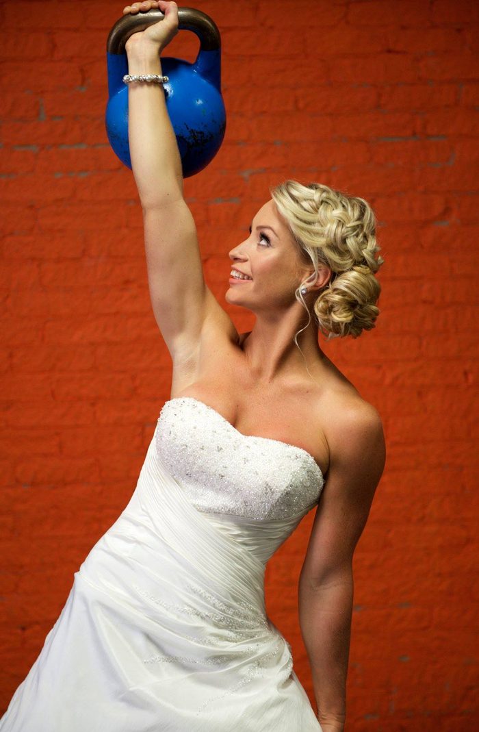 Shannon pressing a kettlebell overhead in a wedding dress — strength meets celebration